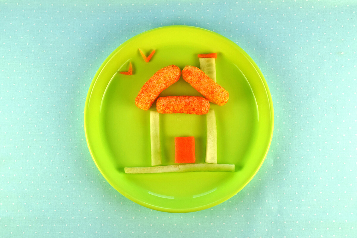 Rectangle of carrot placed within the cucumber square to create a door. V shaped carrot pieces placed above house to create birds