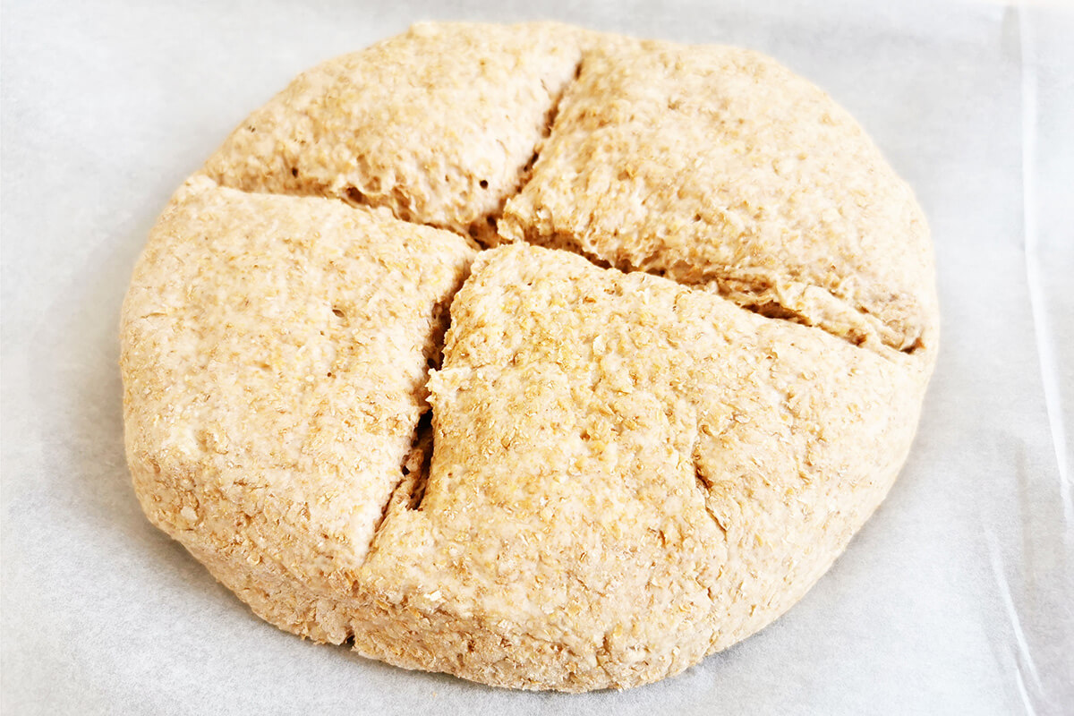 Soda bread dough on a baking sheet with a cross cut across the centre