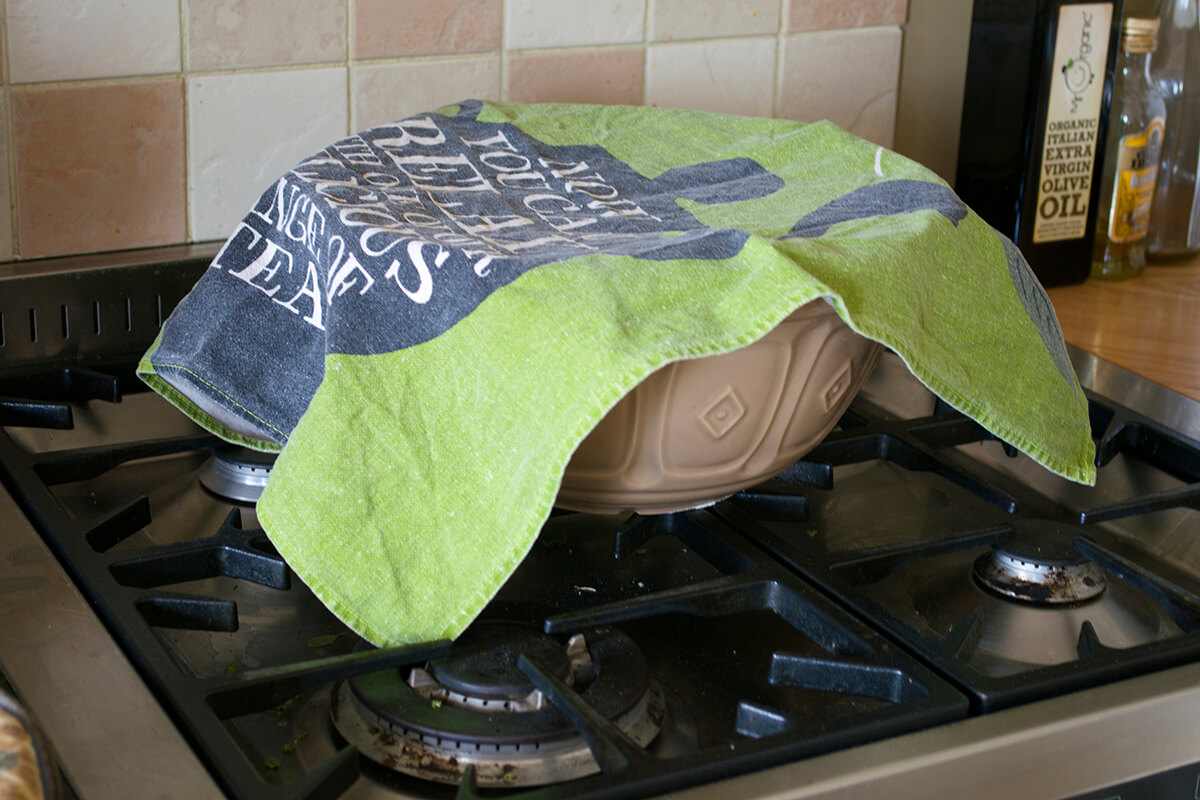 Bread dough resting in a large bowl covered by tea towel 