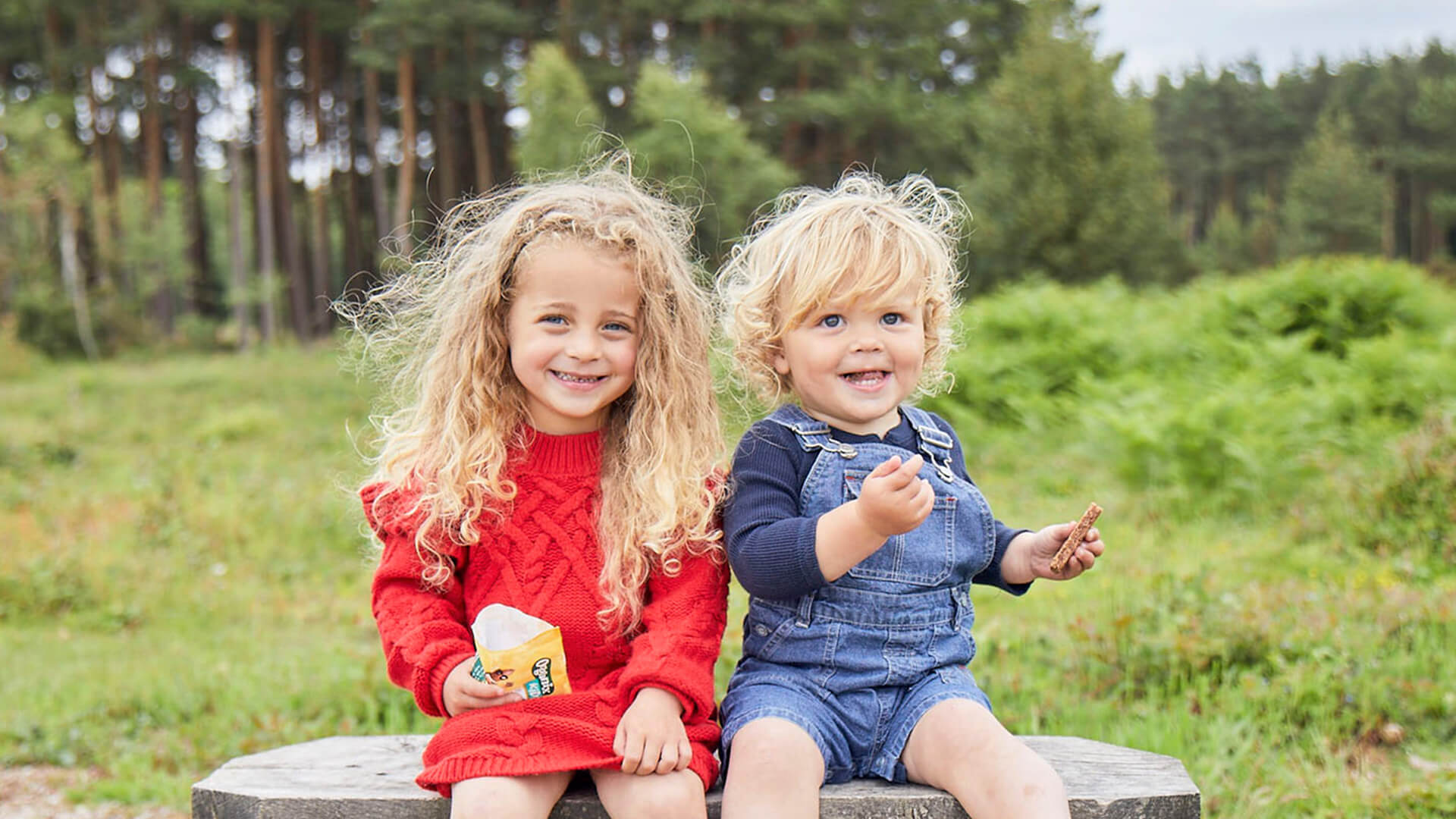 Two toddlers sitting outside, eating Organix snacks