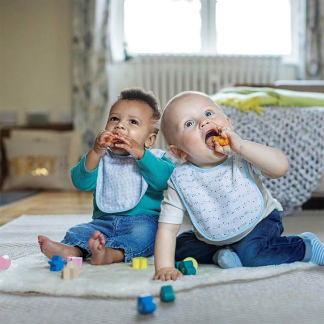 Two babies sitting next to each other and eating