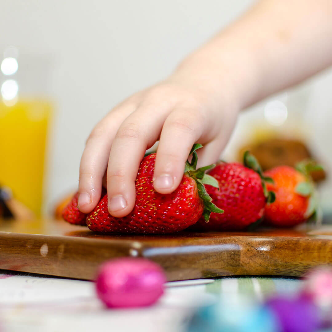 A toddler's hand picking up a strawberry