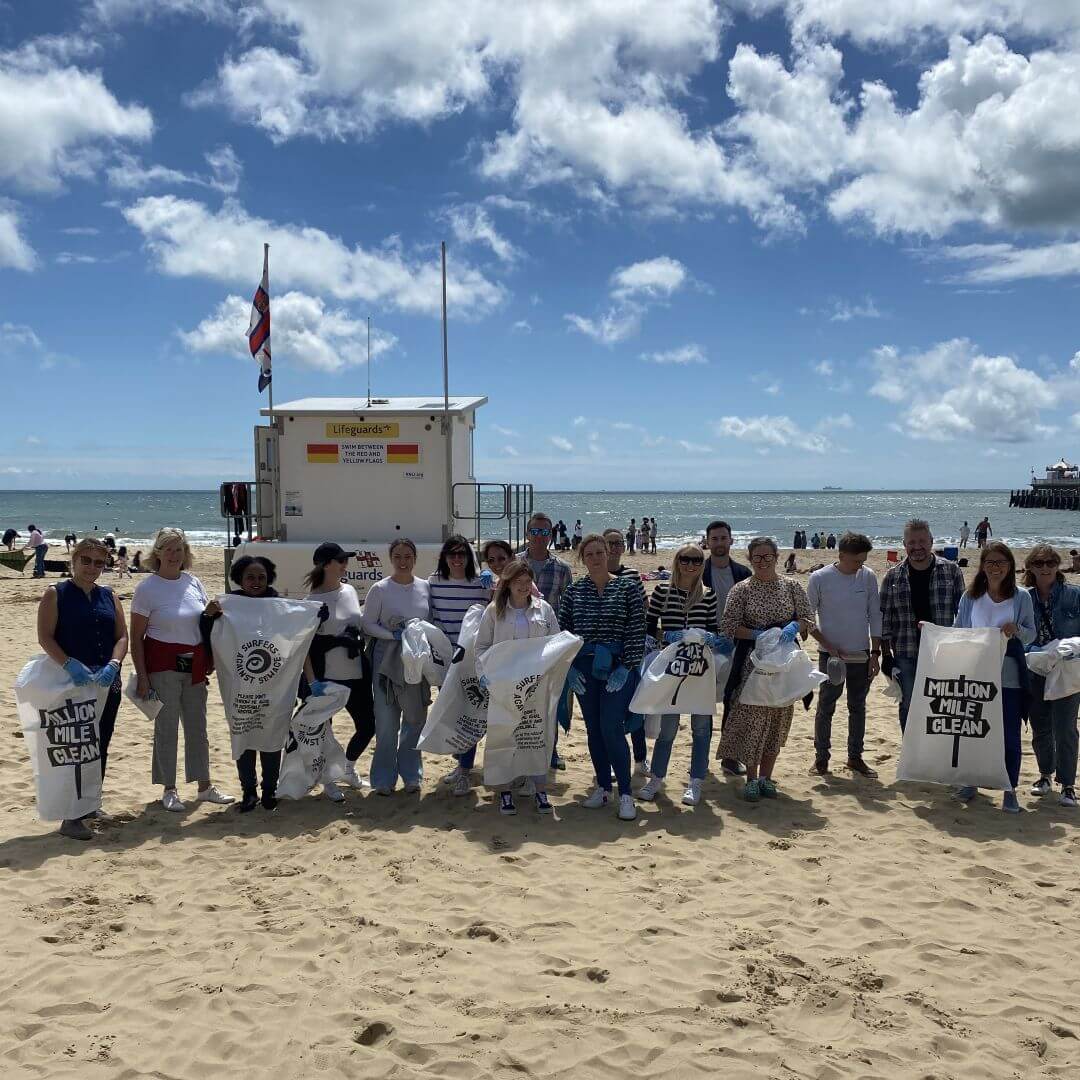 team of people holding white rubbish bags doing a beach clean on golden sand beach with blue sky with clouds